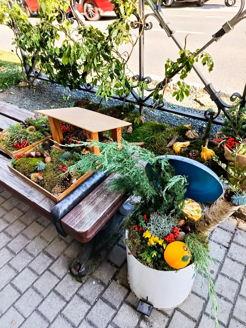 Podzimní výzdoba před školou s přírodními materiály, dýní, květinami a dřevěnou lavičkou.