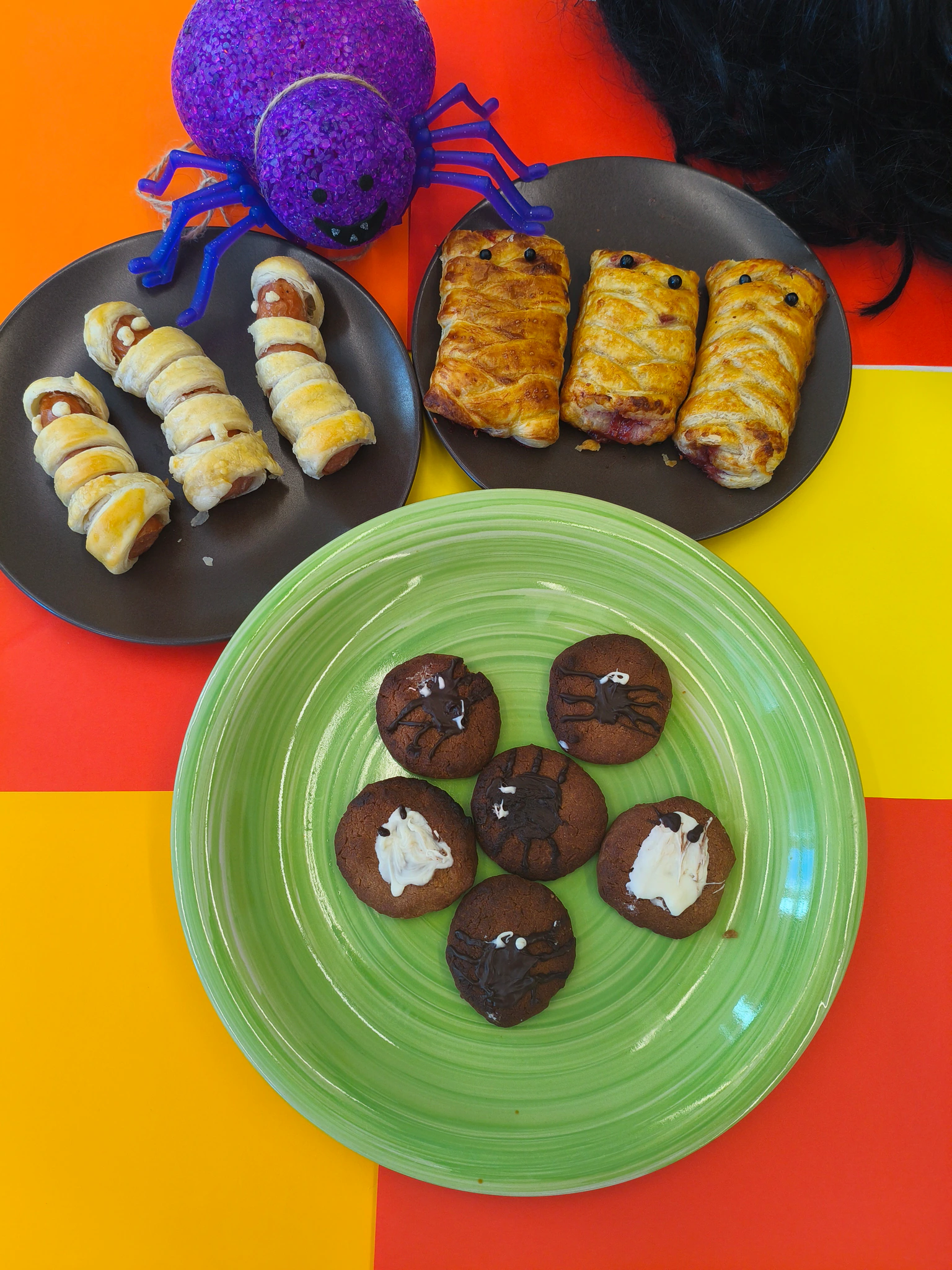 Výběr halloweenských slaných a sladkých dobrot na talířích s pavoučí dekorací.