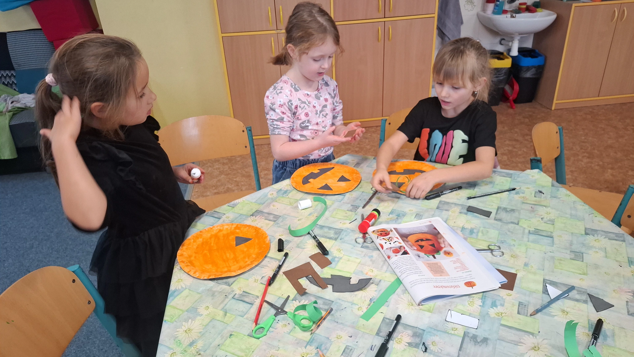 Děti ve školní družině vyrábějí oranžové dýně z papíru a dalších výtvarných materiálů.